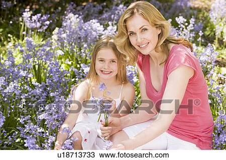 Stock Image - Mother and daughter outdoors holding flowers smiling. Fotosearch