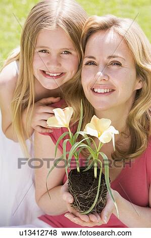Stock Photo - Mother and daughter outdoors holding flower smiling. Fotosearch