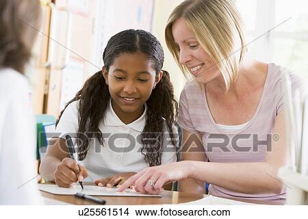 Picture - Student in class taking notes with teacher helping. Fotosearch