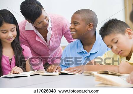 Stock Photo - Students in class reading with teacher helping (selective focus). Fotosearch
