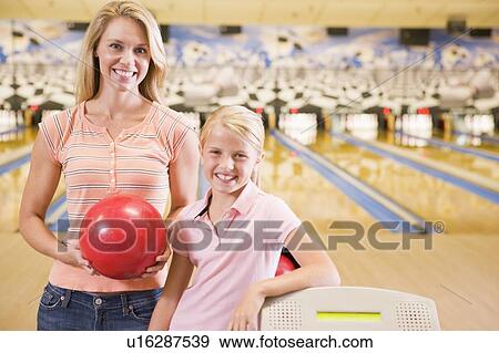 Stock Photo - Woman and young girl in bowling alley holding ball and smiling. Fotosearch