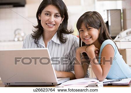 Picture - Woman and young girl in kitchen with laptop and paperwork smiling. Fotosearch