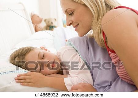 Stock Image - Woman waking young girl in bed smiling. Fotosearch