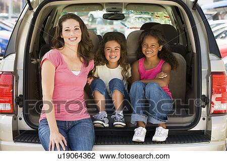 Stock Image - Woman with two young girls sitting in back of van smiling. Fotosearch