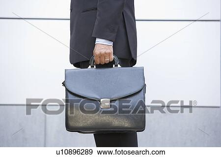 Stock Photo - Businessman holding briefcase outdoors. Fotosearch