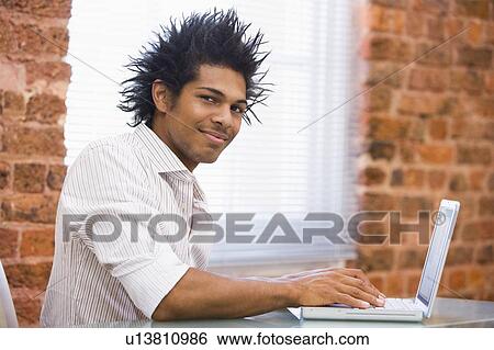 Businessman sitting in office typing on laptop View Large Photo Image Stock Photograph - Businessman sitting in office typing on laptop. Fotosearch
