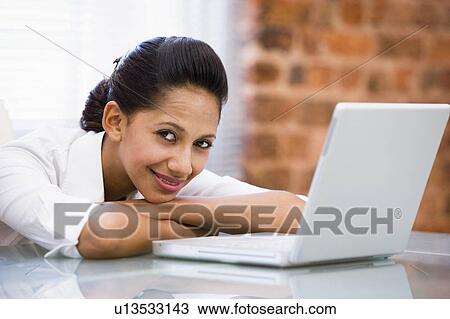 Stock Image - Businesswoman in office with laptop smiling. Fotosearch