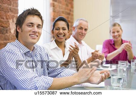 Stock Photo - Four businesspeople in boardroom applauding and smiling. Fotosearch