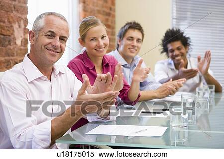 Stock Photography - Four businesspeople in boardroom applauding and smiling. Fotosearch
