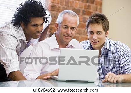 Stock Image - Three businessmen in office looking at laptop smiling. Fotosearch