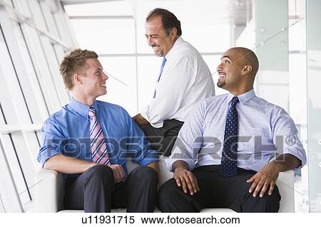 Stock Photography - Three businessmen sitting indoors smiling (high key/selective focus). Fotosearch