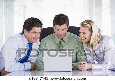 Stock Photography - Three businesspeople in office with laptop smiling. Fotosearch