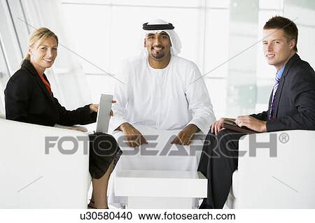 Stock Image - Three businesspeople indoors with a laptop smiling (high key/selective focus). Fotosearch
