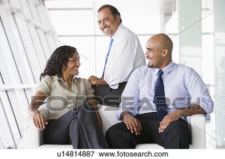 Three businesspeople sitting indoors smiling (high key/selective focus) View Large Photo Image Stock Photo - Three businesspeople sitting indoors smiling (high key/selective focus). Fotosearch