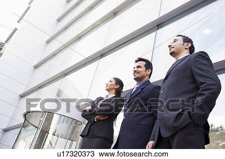 Three businesspeople standing outdoors by building smiling (high key/selective focus) View Large Photo Image Stock Image - Three businesspeople standing outdoors by building smiling (high key/selective focus). Fotosearch