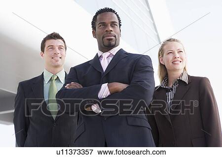Stock Photo - Three businesspeople standing outdoors by building smiling. Fotosearch