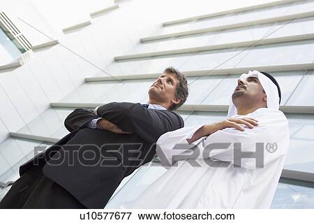 Stock Photo - Two businessmen standing outdoors by building (high key/selective focus). Fotosearch