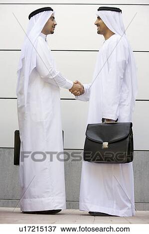 Two businessmen standing outdoors with briefcases shaking hands smiling View Large Photo Image Stock Photo - Two businessmen standing outdoors with briefcases shaking hands smiling. Fotosearch