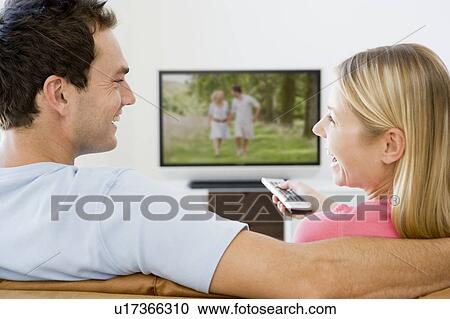 Stock Image - Couple in living room watching television smiling. Fotosearch