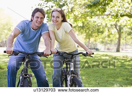 Stock Image - Couple on bikes outdoors smiling. Fotosearch