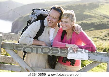 Couple on cliffside outdoors leaning on railing and smiling View Large Photo Image Stock Photo - Couple on cliffside outdoors leaning on railing and smiling. Fotosearch
