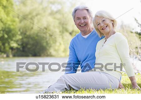 Stock Image - Couple outdoors at park by lake smiling. Fotosearch
