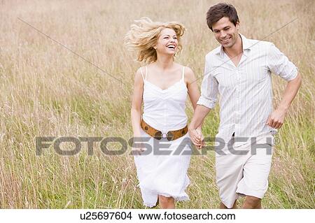 Picture - Couple running outdoors holding hands smiling. Fotosearch