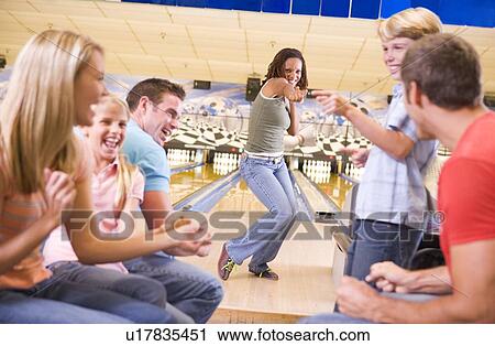 Stock Image - Family in bowling alley with two friends cheering and smiling. Fotosearch