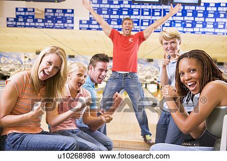 Stock Photo - Family in bowling alley with two friends cheering and smiling. Fotosearch