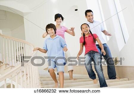 Stock Image - Family running down staircase smiling. Fotosearch