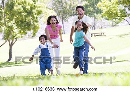Stock Image - Family running outdoors holding hands and smiling. Fotosearch