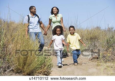 Stock Image - Family walking on path holding hands and smiling. Fotosearch