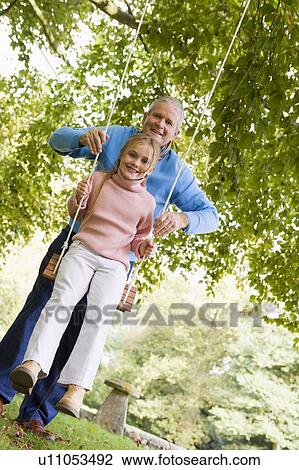 Grandfather pushing granddaughter on swing and smiling (selective focus) View Large Photo Image Stock Image - Grandfather pushing granddaughter on swing and smiling (selective focus). Fotosearch