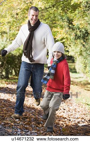 Stock Image - Man and young boy running outdoors in park and smiling. Fotosearch