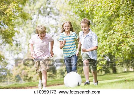Stock Image - Three young friends playing soccer. Fotosearch