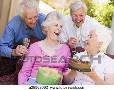 Stock Image - Two couples on patio with cake and gift smiling. Fotosearch