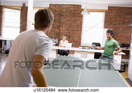 Picture - Two men in office space playing ping pong. Fotosearch