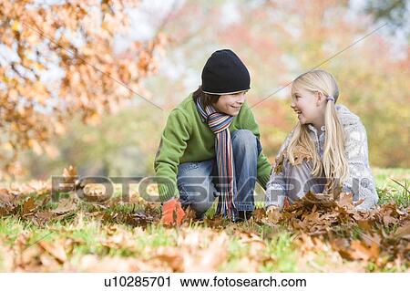 Stock Image - Two young children outdoors in park playing in leaves and smiling (selective focus). Fotosearch