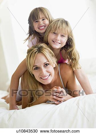 Stock Image - Woman and two young girls in bed playing and smiling. Fotosearch