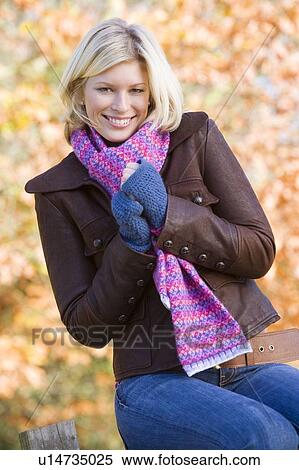 Stock Photography - Woman outdoors at park sitting on fence smiling (selective focus). Fotosearch