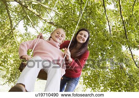 Woman outdoors pushing young girl on swing and smiling (selective focus) View Large Photo Image Stock Image - Woman outdoors pushing young girl on swing and smiling (selective focus). Fotosearch