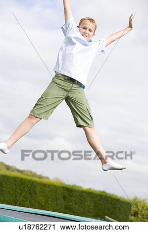 Stock Image - Young boy jumping on trampoline smiling. Fotosearch