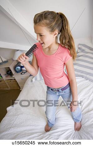 Stock Photography - Young Girl Standing On Her Bed, Singing Into Her Hairbrush. Fotosearch