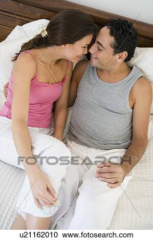 Couple relaxing on bed in bedroom snuggling and smiling (selective focus) View Large Photo Image Stock Image - Couple relaxing on bed in bedroom snuggling and smiling (selective focus). Fotosearch