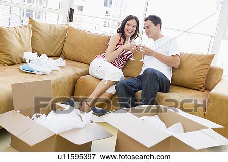 Couple relaxing with champagne by boxes in new home smiling View Large Photo Image Stock Photo - Couple relaxing with champagne by boxes in new home smiling. Fotosearch