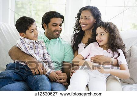 Stock Photo - Family in living room sitting on sofa smiling (high key). Fotosearch