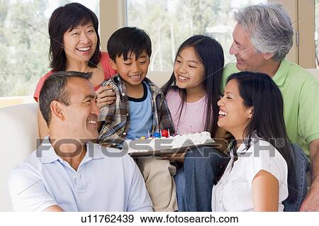 Stock Photo - Family in living room with cake smiling. Fotosearch