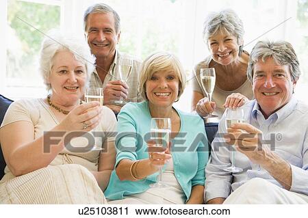 Stock Image - Five friends in living room drinking champagne and smiling. Fotosearch