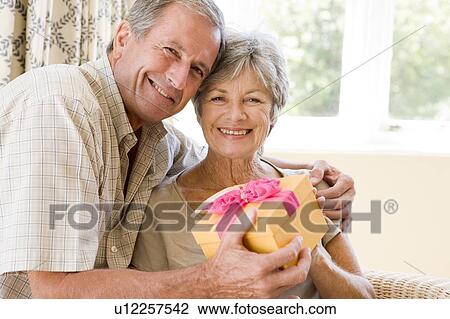Stock Image - Husband giving wife gift in living room smiling. Fotosearch