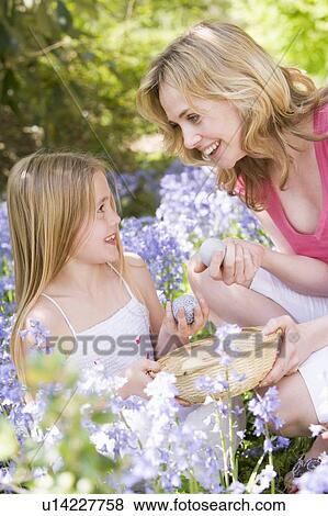 Stock Photo - Mother and daughter on Easter looking for eggs outdoors smiling. Fotosearch